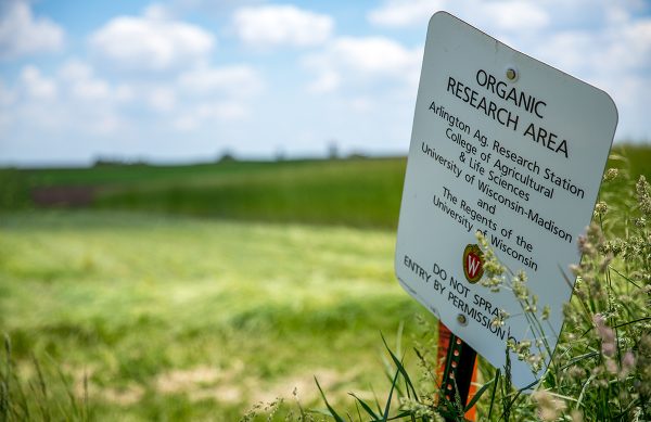 A sign that says Organic Research Area in the foreground, with agricultural research plots in the background.