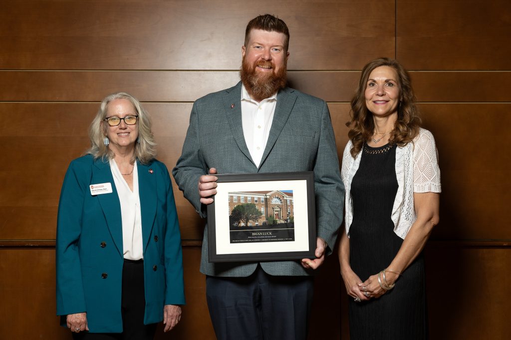 Man standing with award between two women
