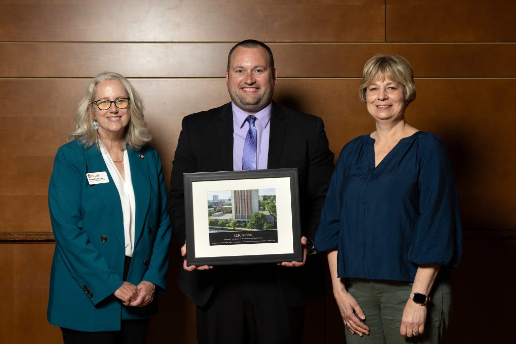 Man with award standing between two women
