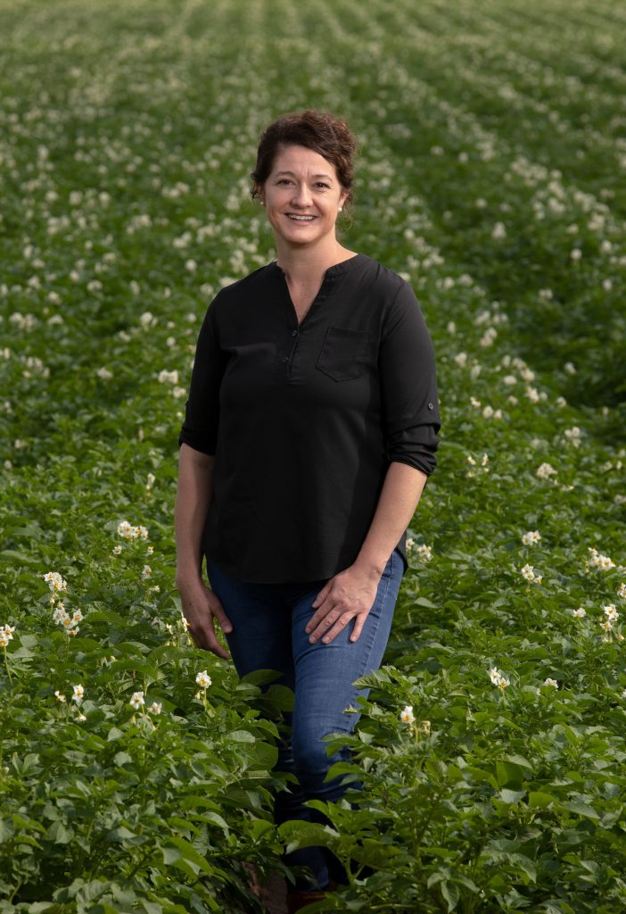 Woman with dark brown hair wearing a black shirt and jeans standing in a potato field