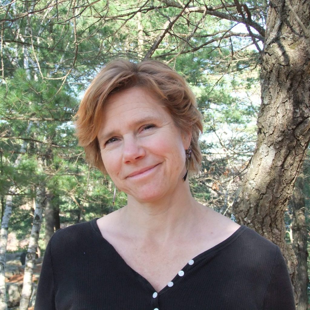 Woman with short, light brown hair wearing a black shirt standing among trees