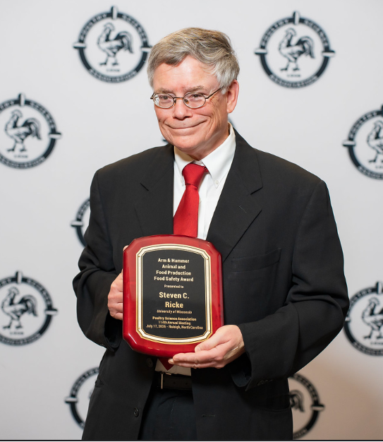 A person in a suit and red tie holding a plaque that reads: 'Arm & Hammer Animal and Food Production Food Safety Award Presented to Steven C. Ricke