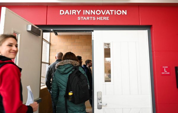 People walk through doorway into building. Sign on building says "Dairy Innovation Starts Here."