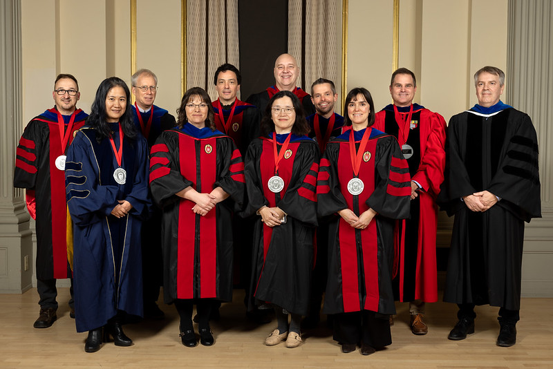 Group of 11 men and women in university regalia standing together, some with medals around their necks.