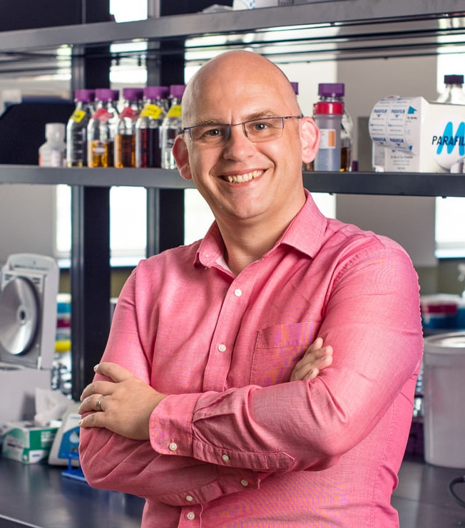 Man in glasses and red shirt standing in front of lab bench