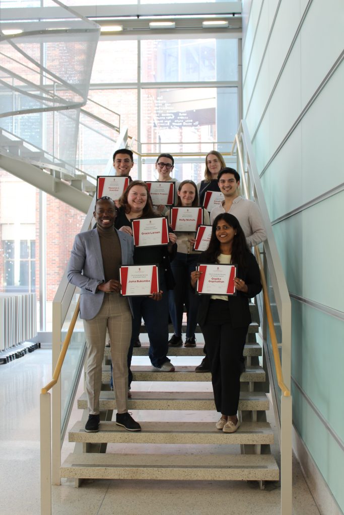 Eight people stand on steps holding certificates