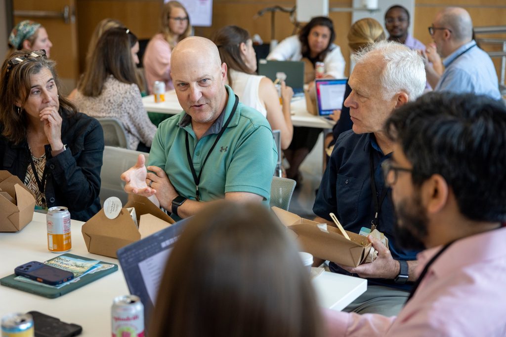 Man in green shirt talks with group of people at at table