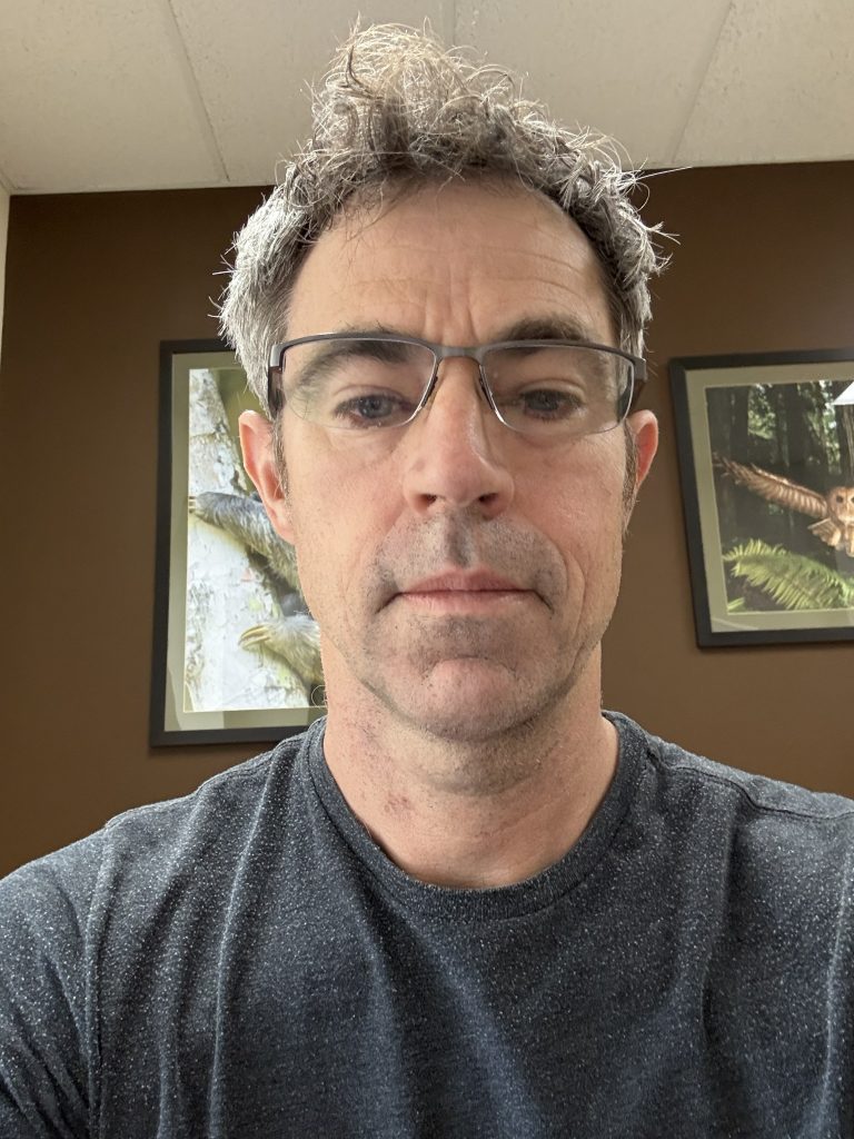 Man with gray hair and glasses looks at camera