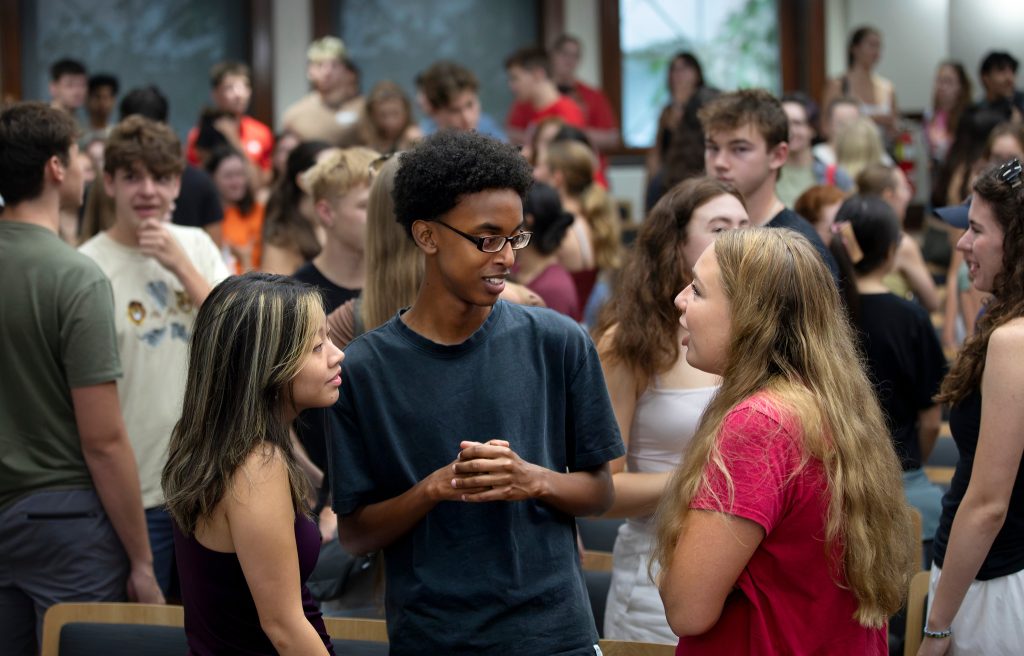 A group of students talk to each other inside a lecture hall
