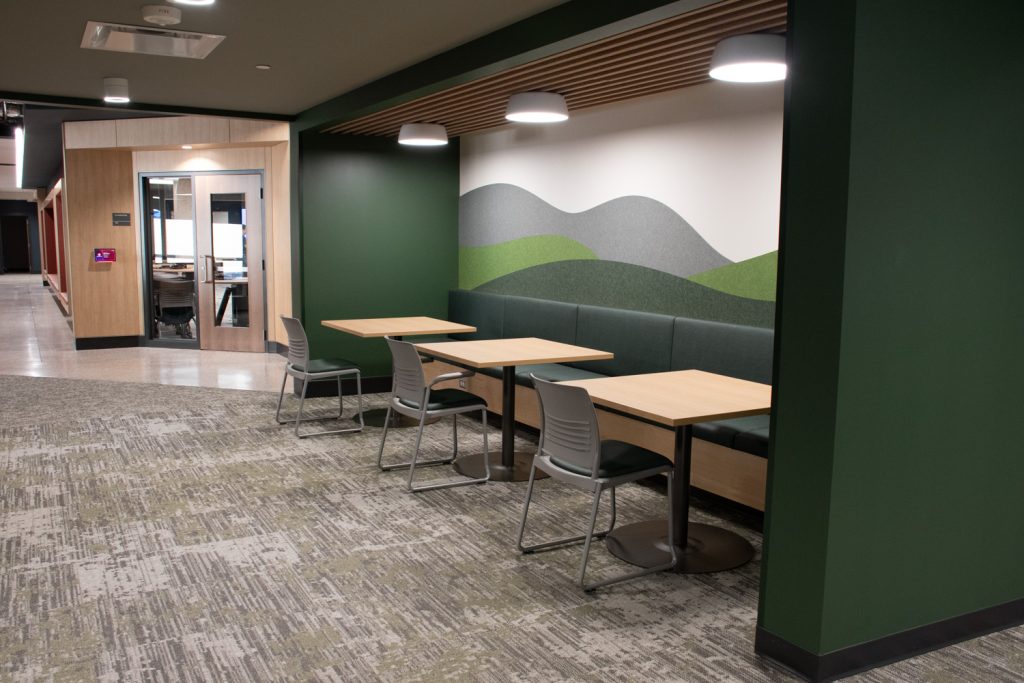 Photos of large space with grey carpet, green walls and three tables in front of hallway and another door.